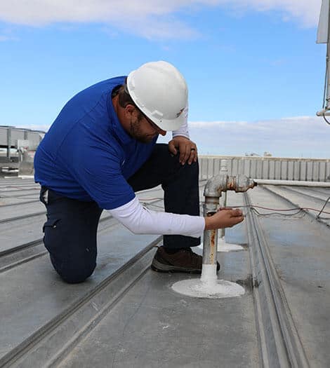 Technician on roof of commercial building repairing a pipe